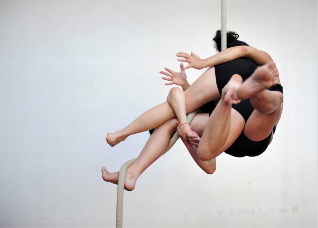Two aerial rope performers are tangled together on the rope
