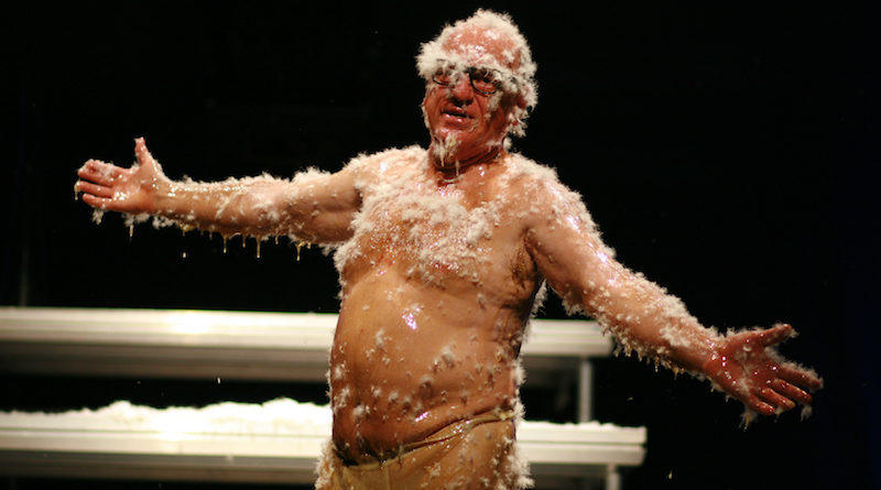 Professional clown Leo Bassi spreads his arms open while covered in honey and feathers