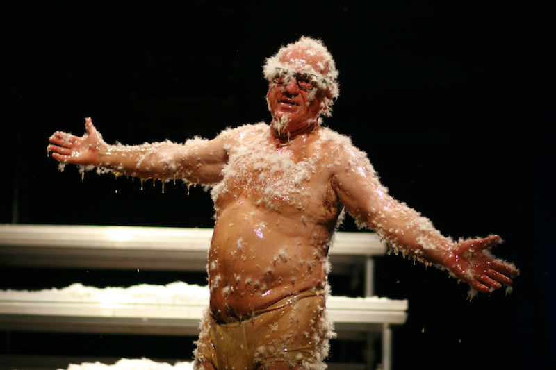 Professional clown Leo Bassi spreads his arms open while covered in honey and feathers