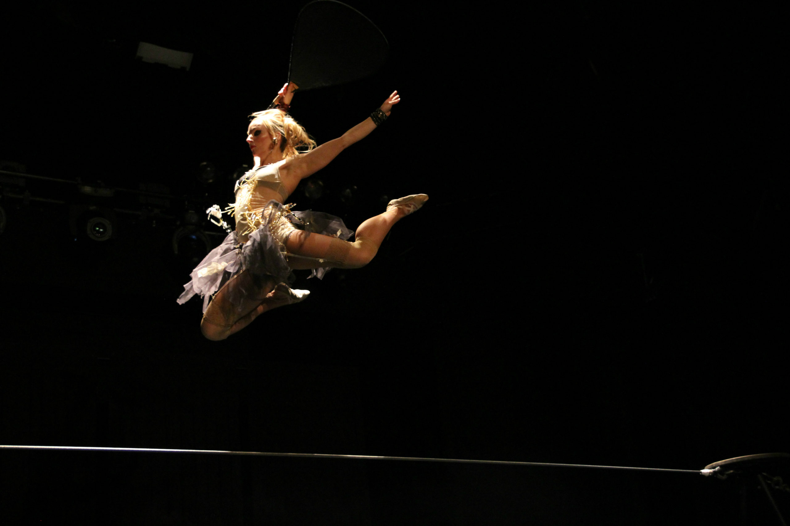 A woman in a skirt performs a dramatic leap on top of the tight wire