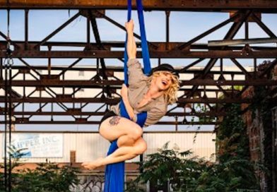 Shannon McKenna sits prettily on a blue aerial silk outdoors