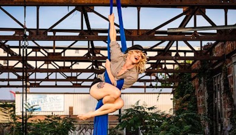 Shannon McKenna sits prettily on a blue aerial silk outdoors
