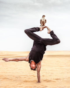 Nicolas Montes de Oca does a handstand in the sand with a bird sitting on his foot