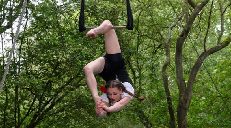 Aerialist pulls her leg over her head hanging from a static trapeze