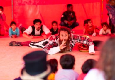 A circus performer lays on the floor, performing a skit for a group of children