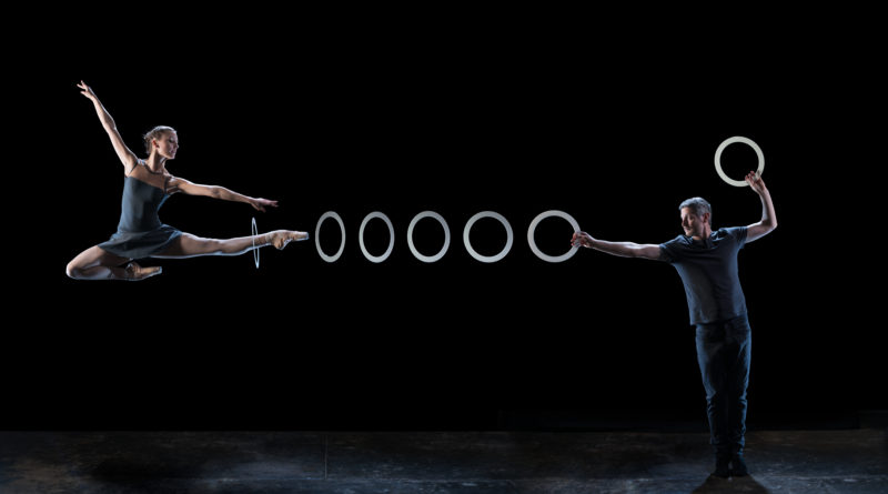 a dancer jumps with a leg extended to the right of the image, a juggling ring is suspended around her ankle a series of juggling rings extend to a circus juggler's hand