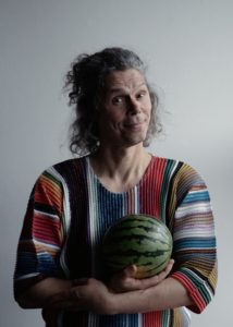 Sean Gandini, circus performer and director, wears a striped shirt and stands holding a small watermelon.