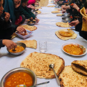 An event for MMCC social circus in Afghanistan. Hungry Afghan children at a long table eat bread and stew 