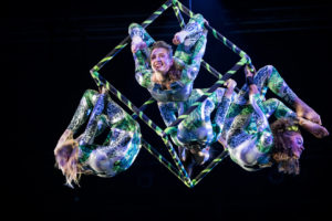 Three aerialists perform on an aerial cube.
