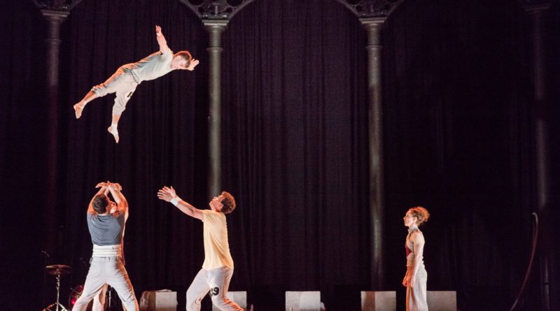 Barely Methodical Troupe in KIN. Four performers onstage. One acrobat stands back as two acrobats prepare to catch a fourth.
