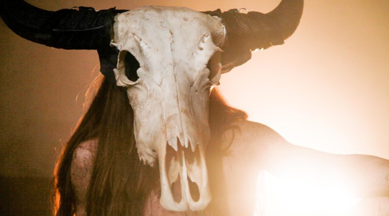 Performer Zinnia Oberski as Wild Woman, wearing a bull skull mask. Wild Woman has long, reddish hair and no clothes