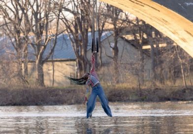 Under Rochester Bridge, Black circus performer Julia Baccellieri holds her dance trapeze and skims the Genesee River's surface with her feet. Part of a photoshoot with Avi Pryntz-Nadworny