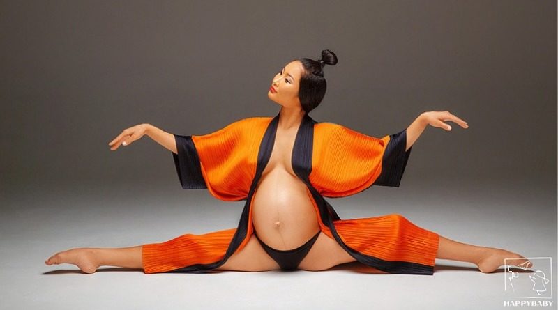 Ulzii Mergen Kee, Mongolian acrobat and circus performer, during pregnancy. She does splits in an open orange robe.