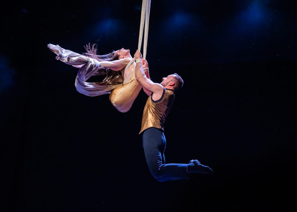 Omnium Circus performers, aerialists Jen Bricker-Bauer and Dominick Baeur. On aerial silks, Dominick holds onto Jen, a legless performer