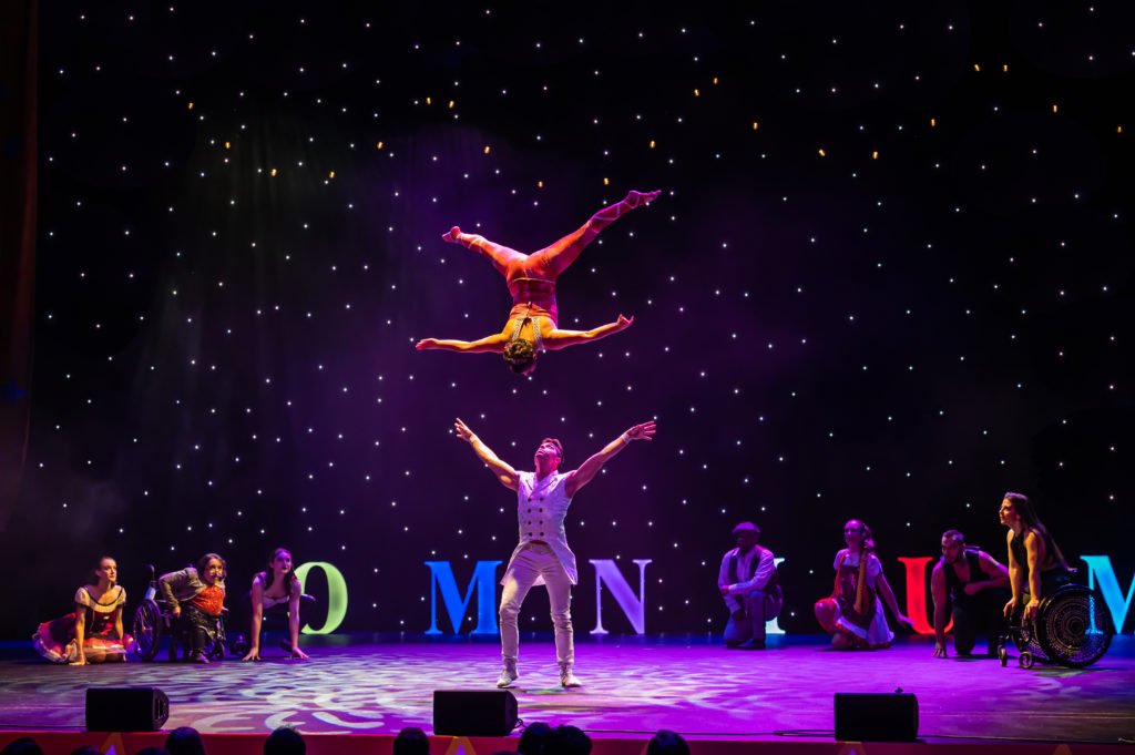 Omnium Circus performers on stage. One male acrobat tosses another into the air