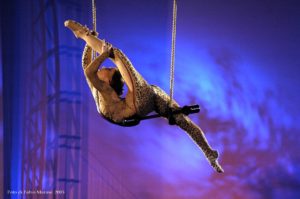 Aurelia Cats, French trapeze artist, poses on a flying trapeze. She pulls one leg above her head.