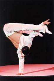 Anatoly Zalievsky, Ukrainian body artist and equilibristic performer, does a one-handed handstand. He wears white acrobatic apparel 