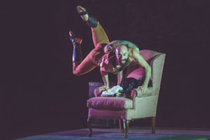 Circus performer Cooper Williams rehearses a static trapeze routine on a red plush chair