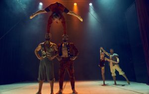 The Losers Cirque Company, five Czech acrobats, onstage. Three male performers form a standing pyramid in the forefront. Behind them, a male and female performer balance together