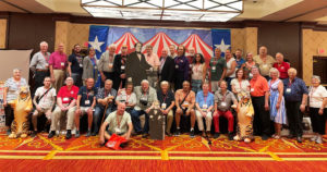 Attendees of the 2022 Circus Historical Society Conference sit for a group photo in front of a circus backdrop and carpet