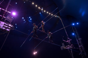 high wire walkers cross a wire in a three person pyramid structure.