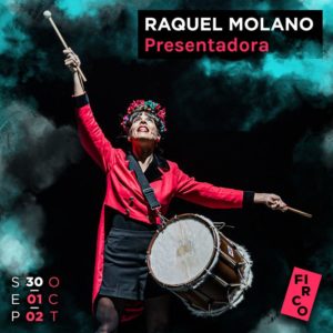Raquel Molano, Spanish actress, plays drums onstage. She wears a red jacket and a red-and-green floral crown