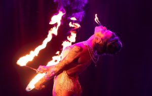 A female fire performer in La Clique does a backbend with two lit torches, blowing flames out of her lips