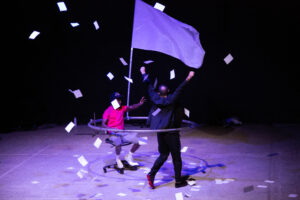 Performers in the contemporary circus show "Pourvu que la mastication ne soit pas longue" depict a scene of police violence with two men in a ring, the dark-skinned man waving a white flag of surrender