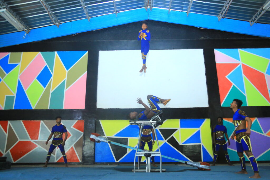 Part of the South Ethiopian circus company Troupe Kolfe, five young men in blue acrobat suits perform Icarian games using a teeter board