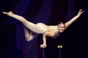 Acrobat Danielle Arata, in costume, performs a one-hand handstand balanced on a single hand block