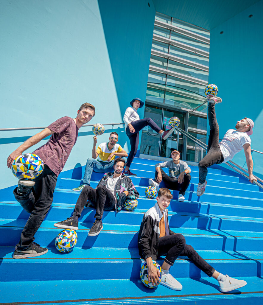 Members of the FootStyle performance company, six young men who play freestyle football, pose with their soccer balls on a large blue staircase
