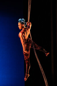 Circus performer Summer Lacy performs on chains against a blue background.