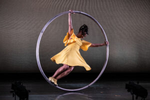 Circus performer Susan Voyticky performs in a yellow dress in a cyr wheel. 