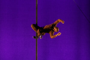 Circus performer Toni Cannon performs on the Chinese pole with a bright purple background.