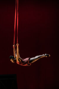 Circus performer Veronica Blair in a red dress performs on red aerial straps. 