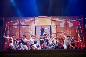 The Taiwanese ensemble of Formosa Circus Art's "Circus Party" show, all in costume, strike poses on a stage with a painted circus tent backdrop