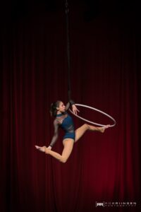 Aerial hoop performer Kalista Russell holds one ankle as she hangs onto the Lyra one-handed
