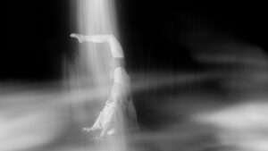 a person in a downward facing dog with one leg raised up in a beam of white light. 