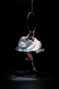 a circus artist spins in a white dress on a lyra