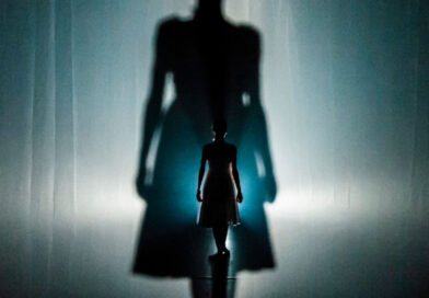 Dancer and performer Erin O'Toole onstage in "Insomniac's Fable" by Agit-Cirk. The backlit Erin is seen from behind.