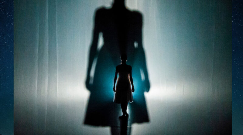 Dancer and performer Erin O'Toole onstage in "Insomniac's Fable" by Agit-Cirk. The backlit Erin is seen from behind.