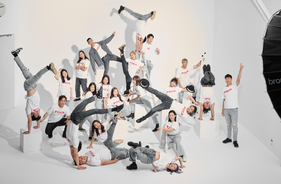 Part of a photo shoot with Taiwan's Formosa Circus Art (FOCA), 21 smiling Taiwanese circus performers in matching T-shirts strike acrobatic poses in the studio
