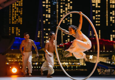 Three Bonfire Circus performers, two young Asian men and a female aerialist in a Cyr wheel, on an outdoor stage at the circus festival Flipside 2023. Some of Singapore's iconic skyscrapers lit up at night are visible in the background.