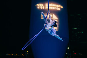 Aerialist, a young Asian woman in an acrobat leotard, performs an aerial straps act at Flipside 2023