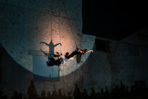 Performing on a rock wall in Elefsina, Greece, a circus artist hangs down from a harness and creates shadow art