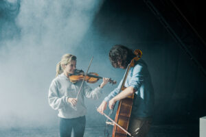 A female violinist and male cellist play together on a foggy stage in Dessa by Creative Sovereignty
