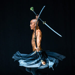 Taiwanese sword dance artist Titos Tsai, a bald Asian man wielding two ornamental swords