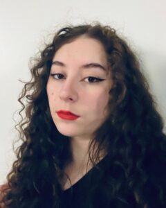 Veronika Agle, a young female circus artist with fair skin, dark brown eyes and curly hair, and red lipstick with cat-eye makeup
