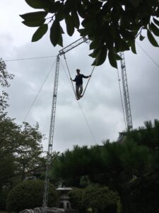 A wire walker prepares for his slackwire act, higher than tree level near the Seto Inland Sea. Setouchi Circus Factory